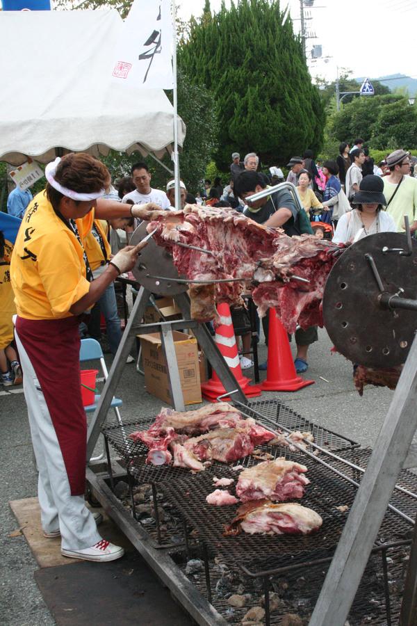 ねじり鉢巻きをした男性が大きな肉の塊を小刀を使って切り落としている写真
