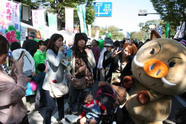 まるいのの着ぐるみの横でベビーカーを押した女性がピースしている写真