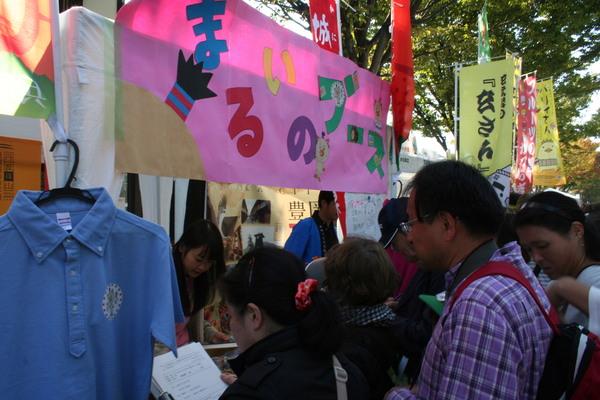 まるいのブースと書かれた露店にお客さん達が集まっている写真