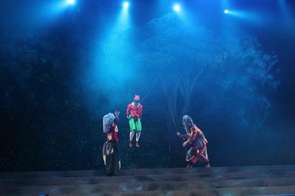 木に吊り下げられたピノキオと両脇に悪さをしている2人がいる写真