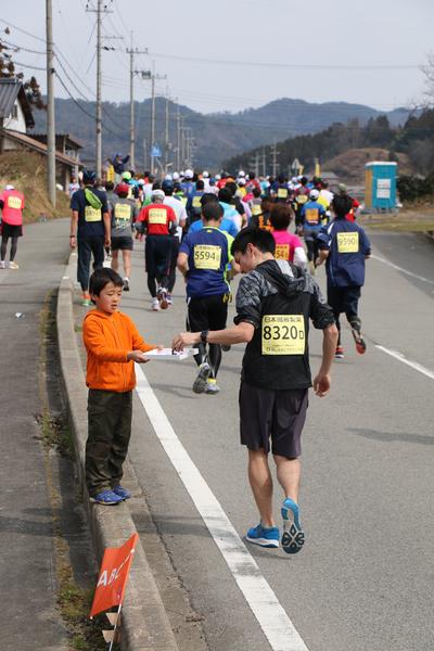 沿道でオレンジのパーカーを来た男の子が箱に入ったお菓子を持って立っていて、男性ランナーが箱からお菓子を取ろうとしている写真