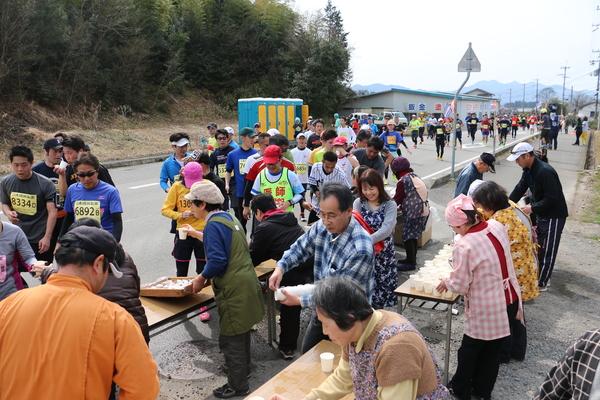 沿道のテーブルに沢山の紙コップが置かれていて、エプロン姿の女性たちがランナー達に飲み物を配っている写真