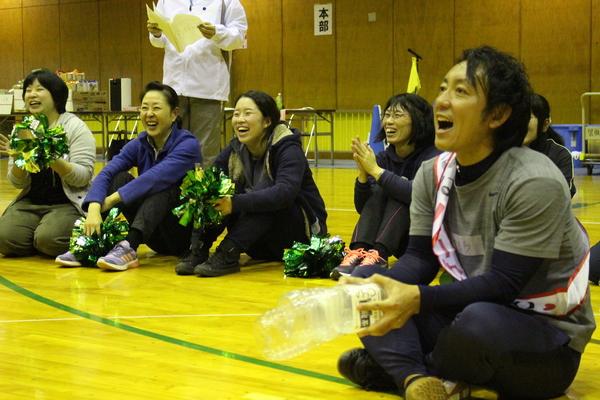 床に座っている職員の方が緑色のポンポンや空のペットボトルを持って、声援を送って応援している様子の写真