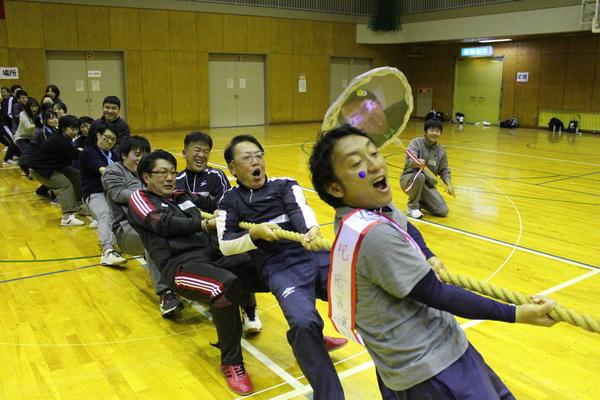綱引きをしている写真で、男性が体を後に傾けて声を合わせて、力いっぱい綱を引いている様子の写真