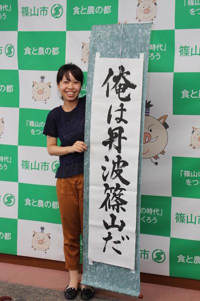 「俺は丹波篠山だ」と習字で書かれた大きな掛軸を女性が持っている写真
