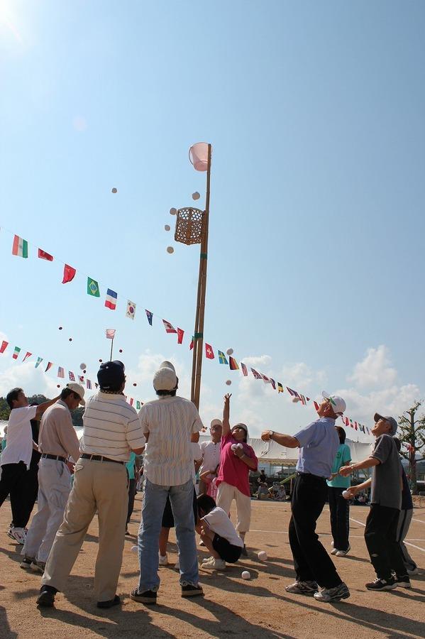 生徒がしゃがんで玉入れの棒を持ち、市長や保護者らが籠に玉を入れている様子の写真