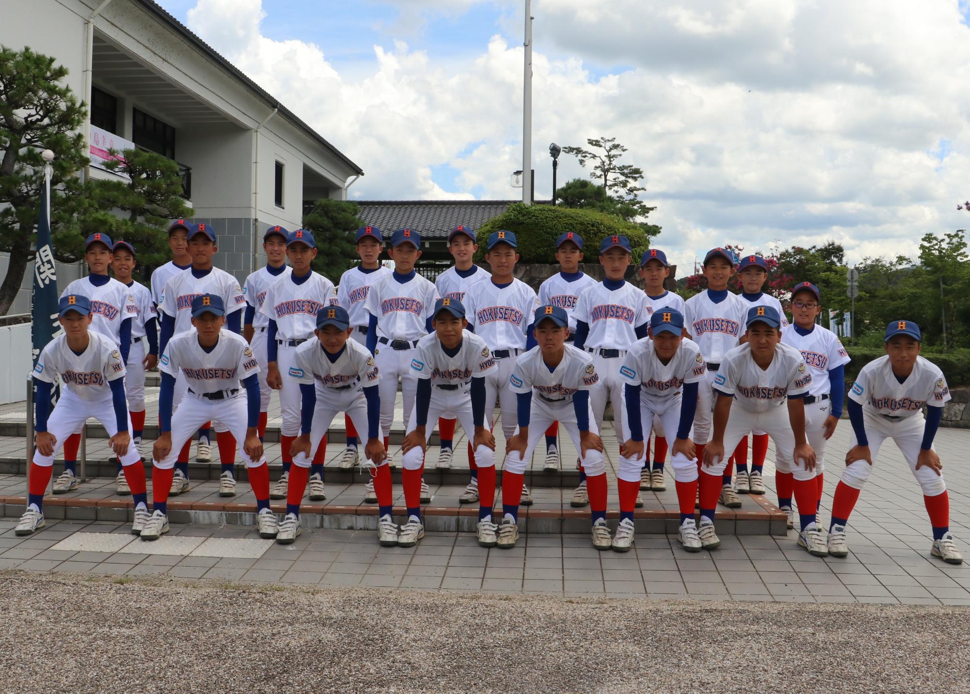 ホール前で、ユニフォームを着た野球チームの子ども達の記念撮影