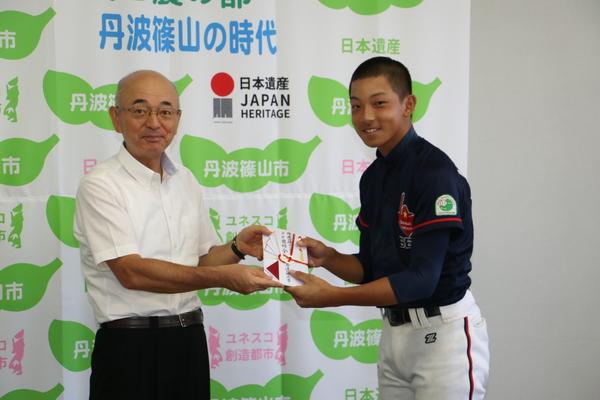 野球のユニフォームを着た男の子が目録を市長と一緒に持っている写真