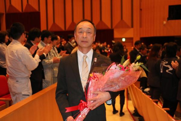 少し寂しげな表情で花束を抱え退場する退職男性の写真