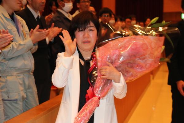 涙を目に浮かべ拍手で送られている女性退職者の写真