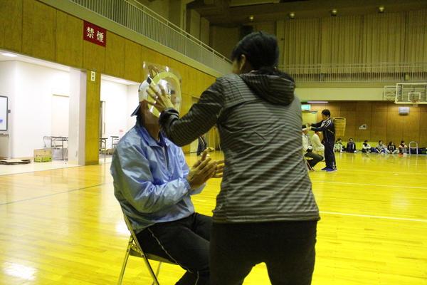 女性が座っている男性にお面をかぶせている写真