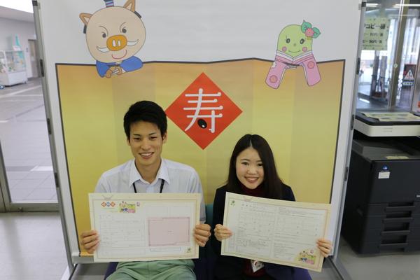 寿と書かれた壁絵の前でカップルがオリジナル婚姻届けを持っている写真