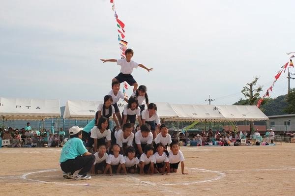 組体操で5段ピラミッドを生徒たちがしており、一番上の生徒がポーズを決めている生徒の写真