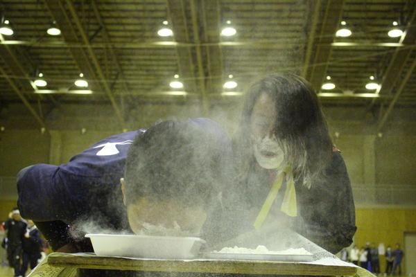 飴食い競争にて、男女ペアで女性は顔が真っ白、男性が飴を探っている写真