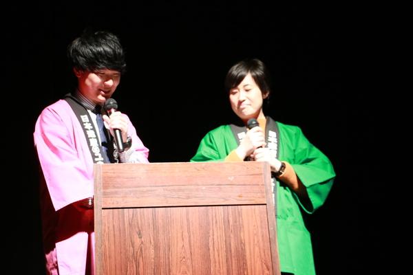 「くろまめカイゼングランプリ2019」イベントにて壇上で男性と女性の司会者がマイクを持っている写真