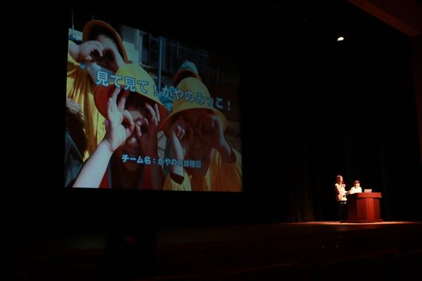 子供たちが笑顔でカメラに向かって写っているスクリーンが映し出されている写真