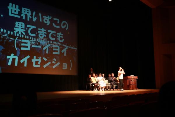 歌っている歌詞がスクリーンに映し出され、スクリーンの前で歌っている女性の写真