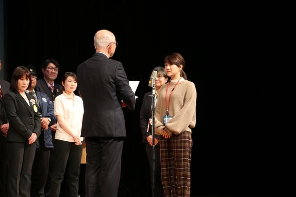 女性の方が表彰され他の職員も壇上に立ち表彰状を読み上げている市長を聞いている写真