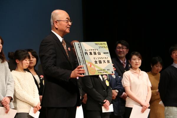 「丹波篠山↔全国大会」と書かれたパネルを見せている市長の写真