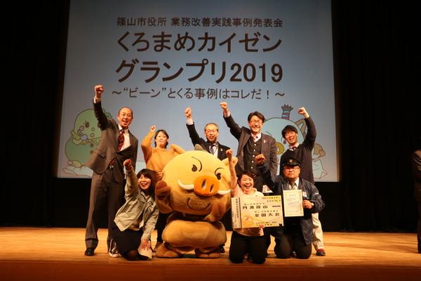 まるいのを中心に皆でオーッ!と記念写真を撮っている商工観光課の職員達の写真