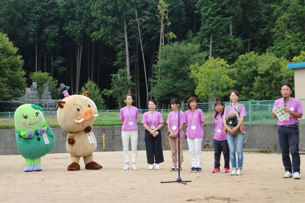 代表理事の鈴木 克哉さんがあいさつして、マスコット人形と職員さんが立ってる写真