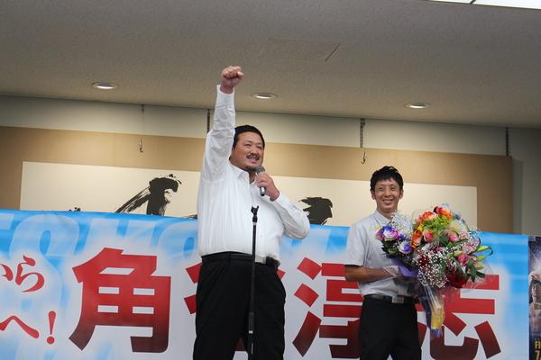 花束を持ち笑顔で写っている角谷 淳志選手と左手でマイクを持ち、右手拳を作り右手を挙げている冴城(さえき)トレーナーの写真