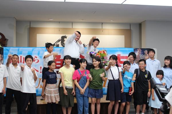 角谷 淳志選手、冴城(さえき)トレーナーの前列で拳を作り手を挙げている子供たちが笑顔で写っている写真