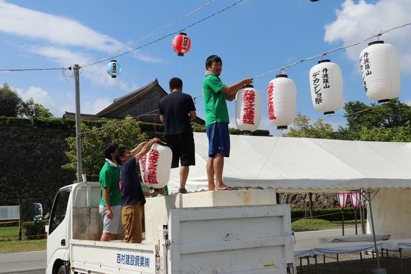 軽トラックの荷台の上の台に乗って祭りの提灯を設置する男性らの写真