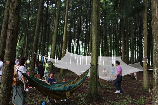 ハンモックに乗っている子供達の姿を大人たちが見守る写真