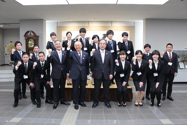 市長と関係者を中心に横2列になり笑顔を見せガッツポーズで記念撮影をしている新規職員達の写真