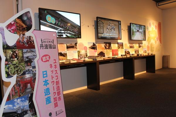3台のスクリーンが壁にかけられその下に並べてある篠山のパンフレットなどがかざられている部屋の写真