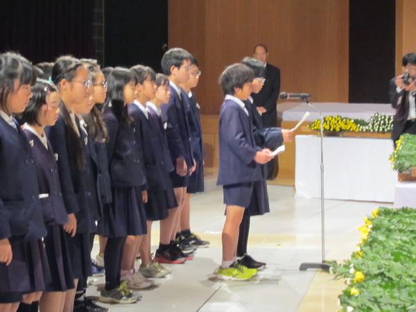 小学生たちが並んでいて、代表の児童がマイクで話をしている写真