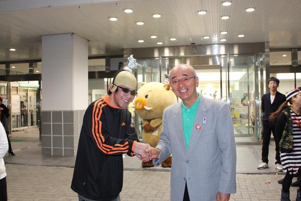 カツラにジャージの男性が市長と握手の写真