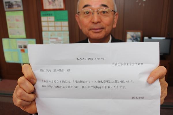 市長が、ふるさと納税についての書類の表紙を両手で持って見せている写真