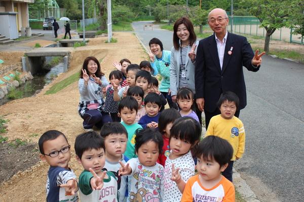 川から上がったところで幼児と先生たち、右端に市長がピースサインをしている集合写真