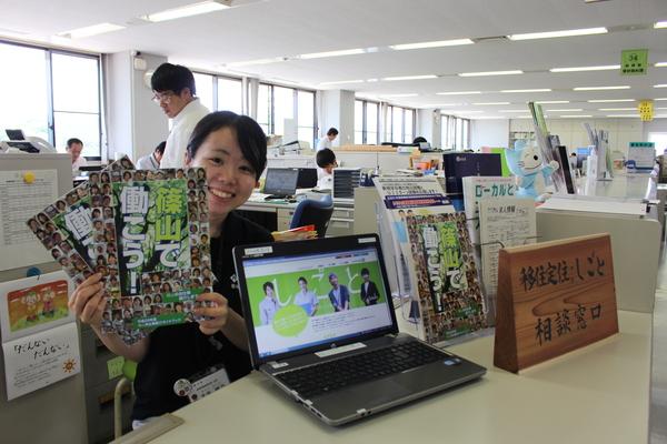 移住定住・しごと相談窓口担当の女性職員が「企業紹介ガイドブック」2冊両手に持って笑顔の写真