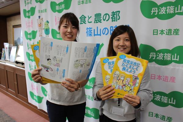 原発災害に備えるハンドブック「原発災害にたくましく備えよう」を手に持った職員2名が写っている写真