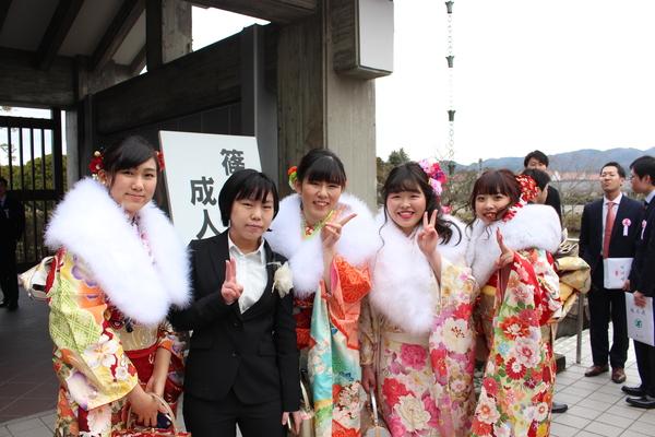 晴れ着姿やスーツ姿の新成人者が成人式会場の入口でVサインをして記念撮影している写真