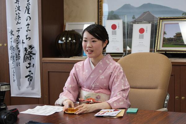 小林さんがお茶の入った透明のグラスに両手を添えて座っている写真