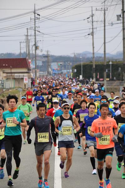 大勢のランナーが沿道を走って、奥の道路にまで連なって走っている写真