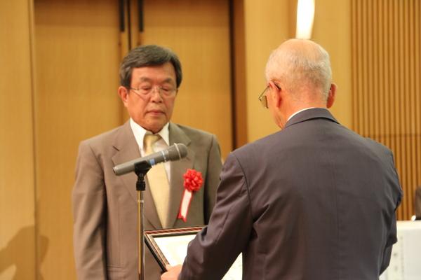 賞状を読み上げる市長の向かい側に立っている男性受賞者を市長の後方から撮った写真