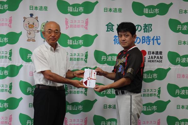 ブラックビーンズの代表の方と市長が目録を手に持ち一緒に記念撮影写真
