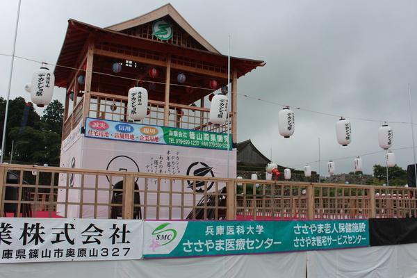 デカンショ祭りの木でつくられた舞台の前に兵庫医科大学ささやま医療センターの幕がかざられている舞台全体完成の写真