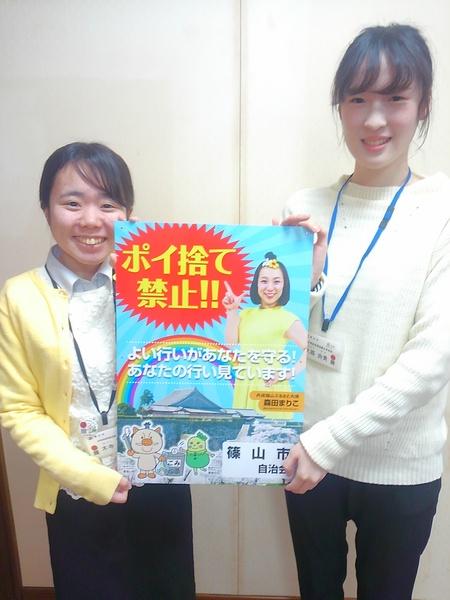 ポイ捨て禁止のポスターをもってこちらに見せている2人の女性職員の写真