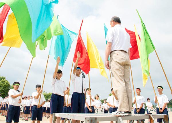 篠山鳳鳴高校の体育祭で、4色の旗を持った生徒たちと、2名の生徒が、片手をあげて選手宣誓をしている写真