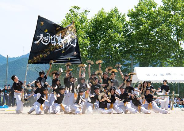 黒いシャツに白いズボンを履いた生徒たちが、黒い旗を持つ生徒の前でセンスを両手に持って上にあげたり、横にしてポーズをとっている写真