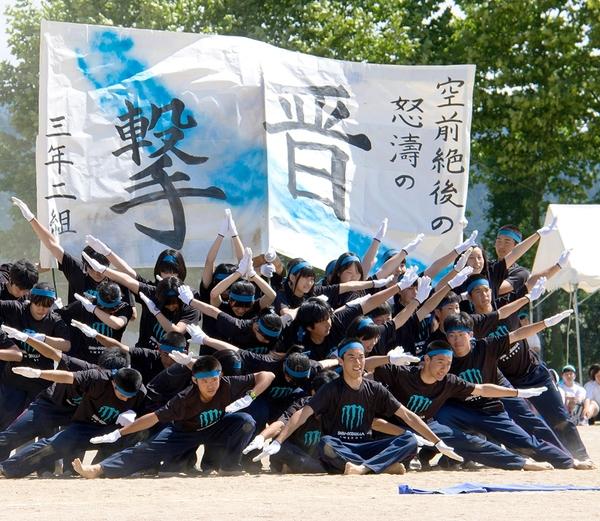 撃晋と大きく書かれた団旗の前で、青いはちまきを巻いた生徒達が、白い手袋はめ頭を下げてポーズをとっている写真