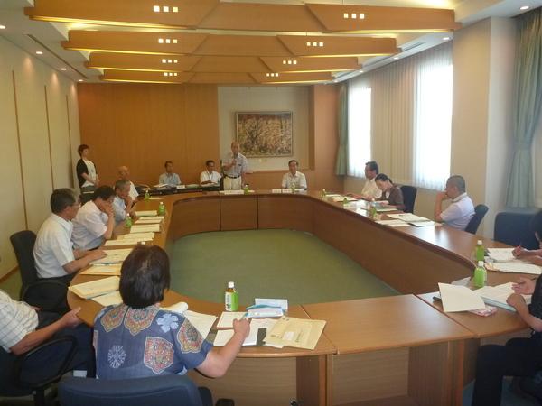 委員会で右手にマイクを持っている中川委員長の話しを聞いている委員メンバーのの写真