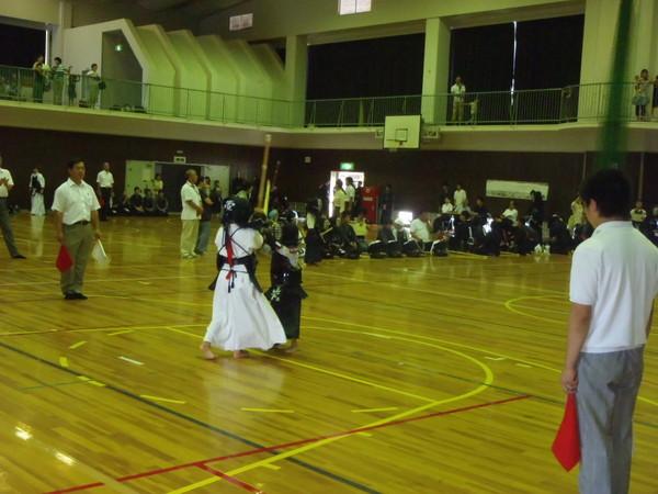 防具をつけた少年2人が剣道の試合をしていて、その周りに赤と白の旗を持った審判が立っている写真