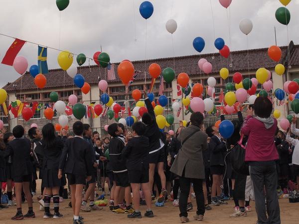 小学生たちが、篠山小学校の校舎で、色とりどりの風船を空高く飛ばしている写真
